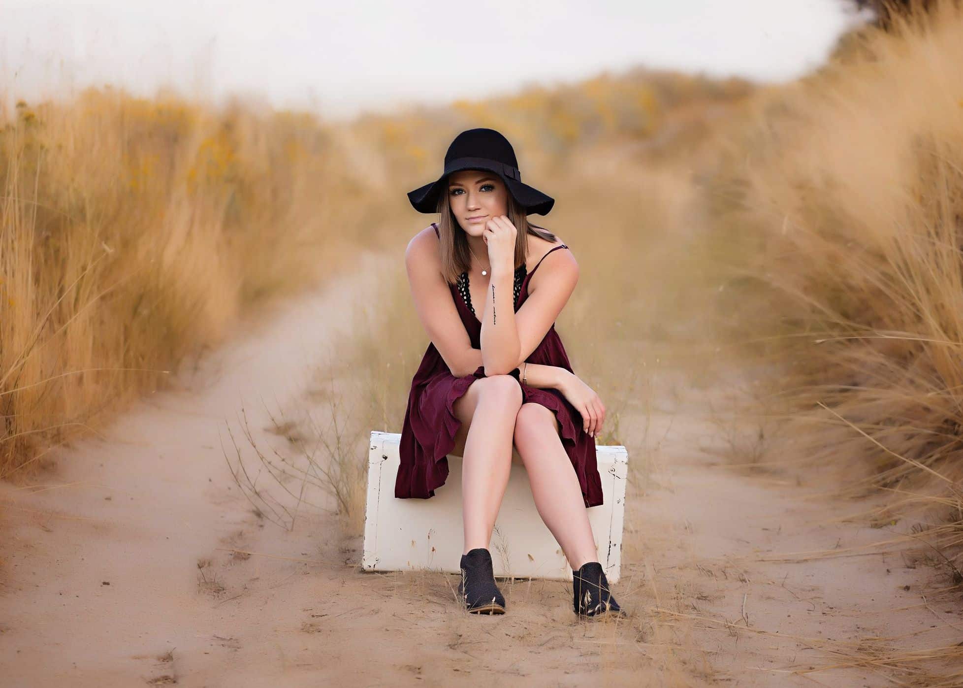 A girl in a tan field sitting on a white box posing for the camera.