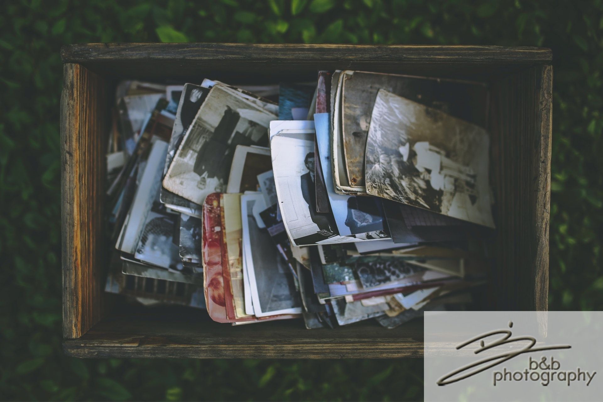 A stack of old photos in a wooden crate against a green background