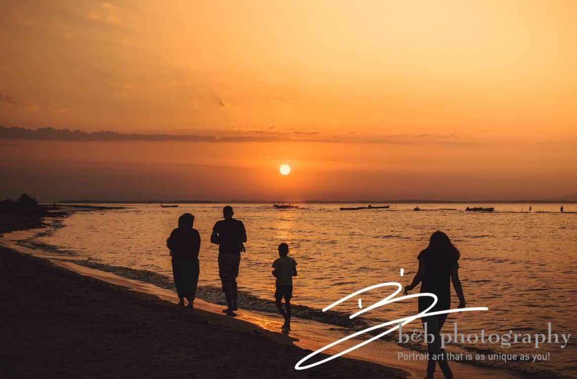 Family of 4 walking along a beach during the sunset.